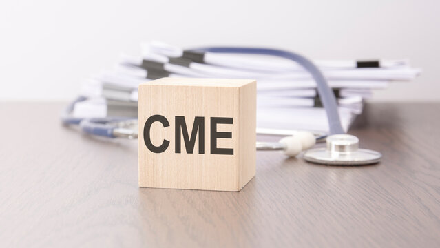 text cme is written on wooden cube near a stethoscope on a dark background