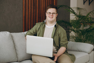 Young IT man with down syndrome wears casual clothes work hold use laptop pc computer sits on grey...