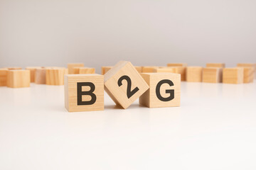 three wooden cubes with B2G symbols on them. white background. in the background there are many wooden blocks of different sizes