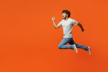 Fototapeta na wymiar Full body side view young overjoyed excited cool smiling happy Indian man wears t-shirt casual clothes jump high run fast isolated on orange red color background studio portrait. Lifestyle concept.