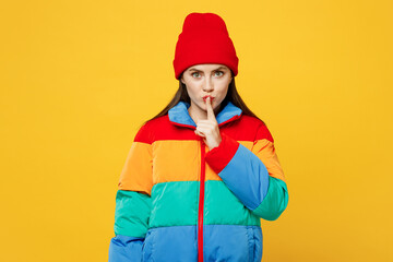 Young secret woman she wears padded windbreaker jacket red hat casual clothes say hush be quiet with finger on lips shhh gesture isolated on plain yellow background studio portrait. Lifestyle concept. © ViDi Studio