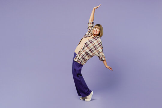 Full body elderly blonde woman 50s years old wear beige t-shirt shirt casual clothes stand on toes leaning back with outstretched hands isolated on plain pastel purple background. Lifestyle concept.
