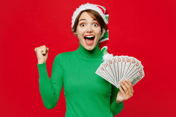 Young woman wear green turtleneck Santa hat posing hold in hand fan of cash money in dollar...