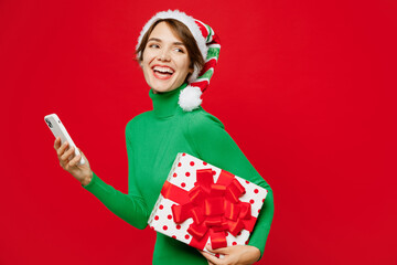 Full body young woman wears green turtleneck Santa hat posing hold mobile cell phone present box...