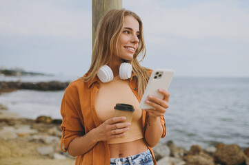 Young happy woman wears orange shirt casual clothes headphones listen to music use mobile cell...