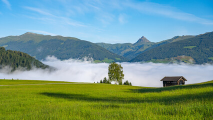 Alpine mountain landscape with green meadows, rural hayloft and Grosser Rettenstein Mountain on...