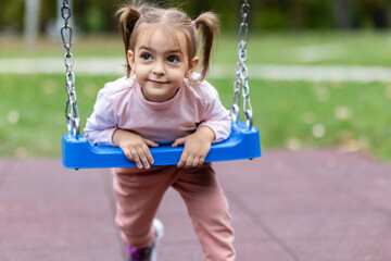 Cute little girl on swing in public park.