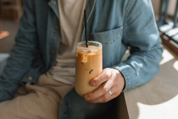 Close-up of a man sitting in a cafe holding a glass of iced coffee