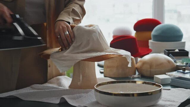 Selective focus of unrecognizable female hat-maker ironing hat on wooden mannequin through cheesecloth