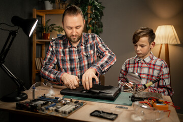 Happy boy and his father sitting together and repairing motherboard using soldering iron. Family...
