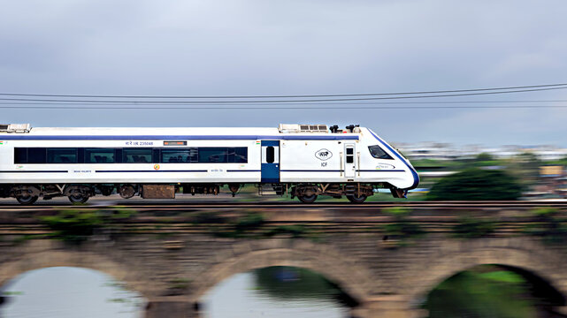 Pune, Maharashtra, India-September 19th, 2023: Pan image of India's first indigenous development semi high speed Vande Bharat , speeding over bridge.