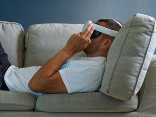 Man using virtual mixed reality glasses, lying down on sofa.