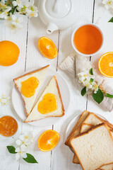 Delicious toast with butter and orange jam and tea on a white wooden background with flowers and fruits. Excellent breakfast.