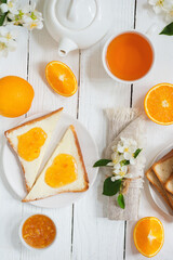 Delicious toast with butter and orange jam and tea on a white wooden background with flowers and fruits.