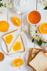 Delicious toast with butter and orange jam and tea on a white wooden background with flowers and fruits.