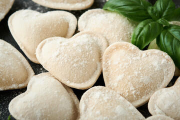 Italian ravioli pasta in heart shape. Tasty raw ravioli with flour and basil on dark background. Food cooking ingredients background. Valentines or Mothers Day lunch ideas. Top view with copy space.