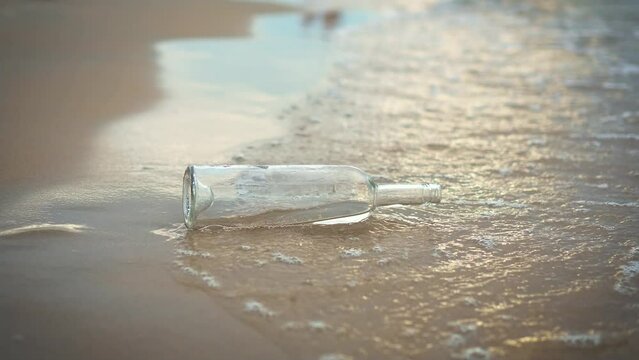 Empty glass wine bottle in water on sand beach at sunset. Ecological garbage catastrophe for nature
