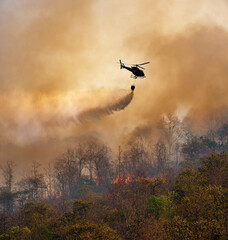 Fire fighting helicopter dropping water onto wildfire because climate change and global warming is...