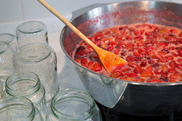 Cooking strawberry jam in a large bowl at home. Wooden spoon in a bowl with jam.Empty glass jars for jam.