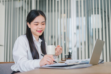 Successful Asian businesswoman looks confident and smiles while working with laptop in office.