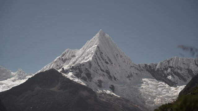 ice covered glacier of a pyramid shaped mountain at laguna paron lagoon in the high andes mountains of the cordillera blanca at huascaran, Peru, with snow covered mountain peaks on a bright sunny day.