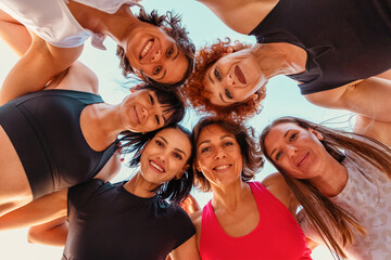 Bottom view of circle group of Caucasian happy smiling women wearing sports clothes looking in...