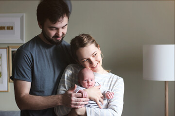 Young parents couple holding and hugging infant baby tenderly at home. Happiness and love concept