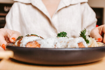 Woman holding a plate of sushi on a table. Photo taken in a food court.