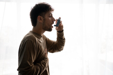 Indian guy suffering from asthma, Young man having asthma using the asthma inhaler for being healthy - obrazy, fototapety, plakaty