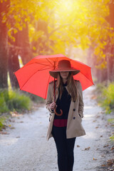 A young woman walks with a red umbrella on a sunny autumn day.