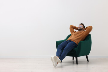 Handsome man relaxing in armchair near white wall indoors, space for text - Powered by Adobe