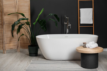 Fototapeta premium Spa day. Ceramic tub, houseplant and wicker table in bathroom