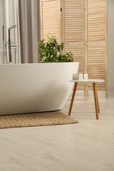 Spa day. Stylish bathroom with ceramic tub, houseplant and wooden side table