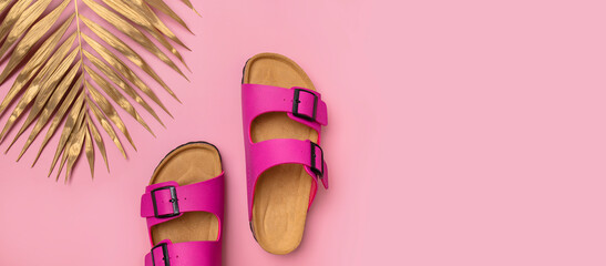 Fashionable leather bright pink birkenstock sandals, golden palm leaf on pink background, top view...