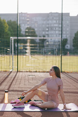 Young woman resting on sporty mat after training on the sports ground.
