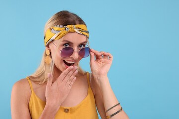 Portrait of smiling hippie woman in sunglasses on light blue background. Space for text