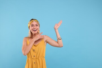 Portrait of happy hippie woman showing at something on light blue background. Space for text