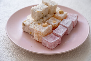 Turkish delights with hazelnuts, pistachios, walnuts, coconut and roses on a pink plate
