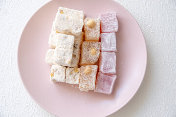 Turkish delights with hazelnuts, pistachios, walnuts, coconut and roses on a pink plate
