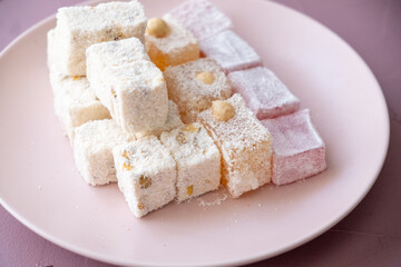 Turkish delights with hazelnuts, pistachios, walnuts, coconut and roses on a pink plate

