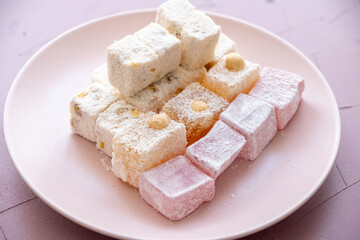 Turkish delights with hazelnuts, pistachios, walnuts, coconut and roses on a pink plate
