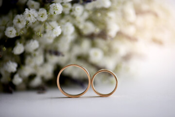 Beautiful gold wedding rings close-up, lying edge to each other on a white surface against a background of white flowers. Wedding. The engagement. Wedding bouquet