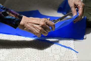 Adult woman's hands cutting a blue fabric with scissors.