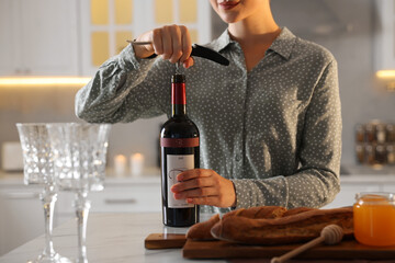 Romantic dinner. Woman opening wine bottle with corkscrew at table in kitchen, closeup