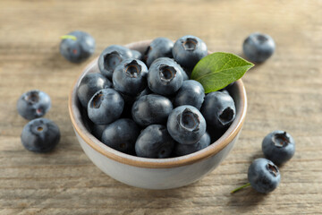 Bowl of tasty fresh blueberries on wooden table, closeup