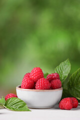 Tasty ripe raspberries and green leaves on white wooden table outdoors, space for text