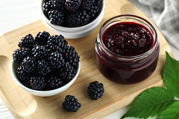 Fresh ripe blackberries, tasty jam and leaves on wooden board, closeup