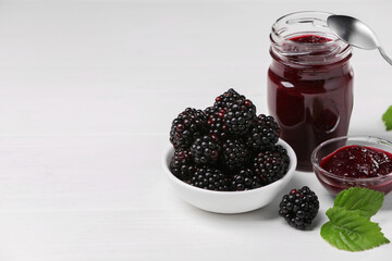 Fresh ripe blackberries, tasty jam and leaves on white wooden table. Space for text