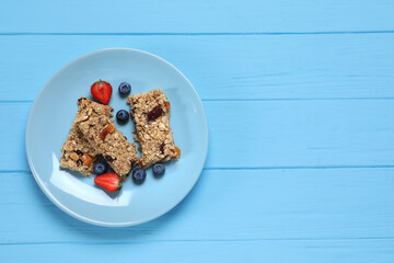 Tasty granola bars with berries on light blue wooden table, top view. Space for text