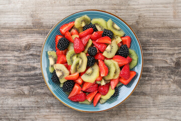 Plate of delicious fresh fruit salad on wooden table, top view